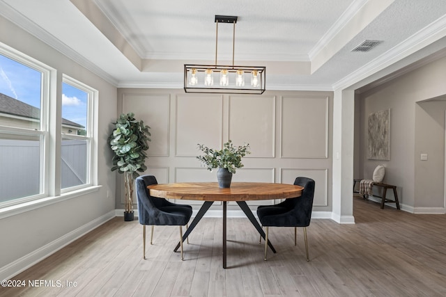 dining space featuring wood-type flooring, a raised ceiling, and crown molding