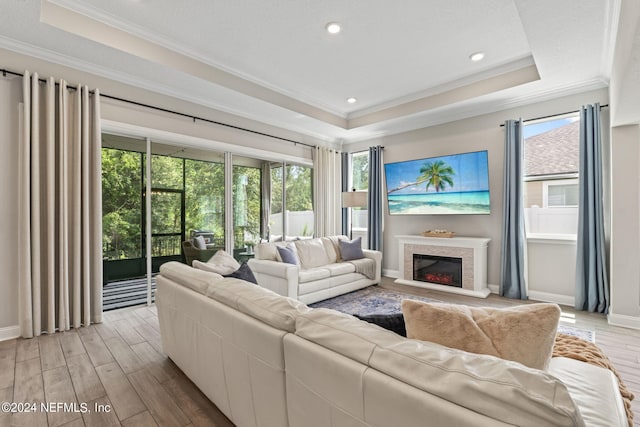 living room featuring a raised ceiling, light hardwood / wood-style flooring, a wealth of natural light, and ornamental molding