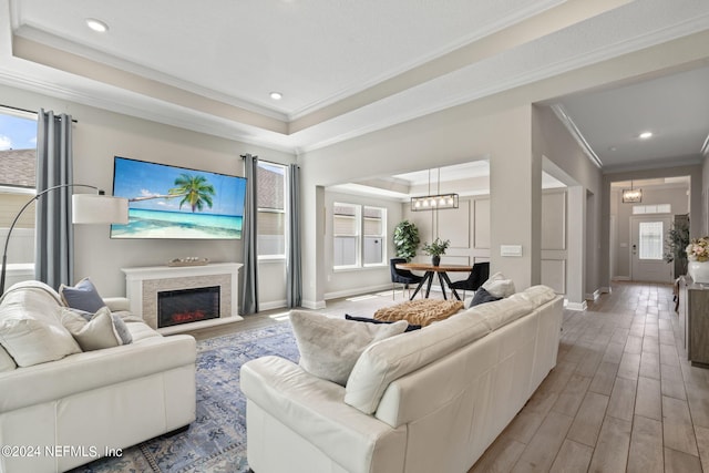 living room featuring a chandelier, crown molding, a tray ceiling, and light hardwood / wood-style flooring