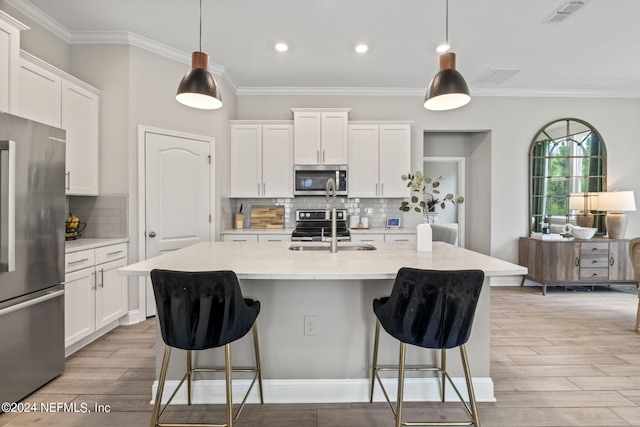 kitchen featuring a kitchen island with sink, white cabinets, decorative light fixtures, and appliances with stainless steel finishes