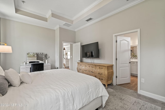 bedroom with a tray ceiling, crown molding, connected bathroom, and light carpet