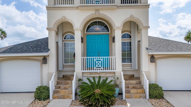 view of exterior entry featuring stucco siding, roof with shingles, and an attached garage