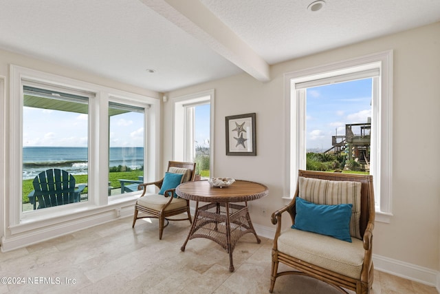 living area with a textured ceiling, beam ceiling, light tile patterned flooring, and a water view