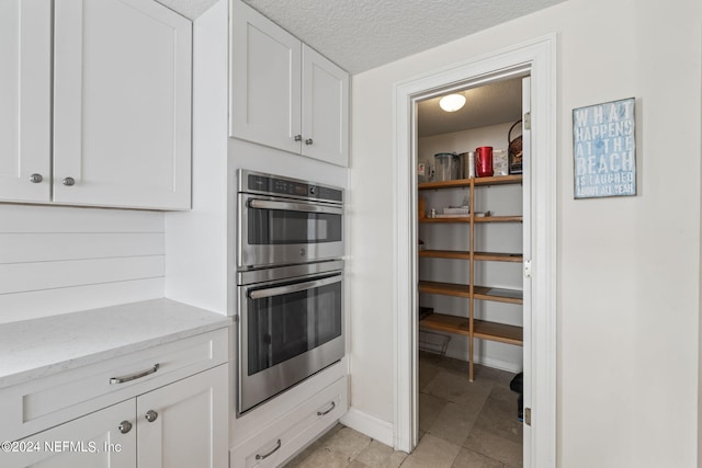 kitchen with white cabinets, light tile patterned floors, a textured ceiling, light stone counters, and stainless steel double oven