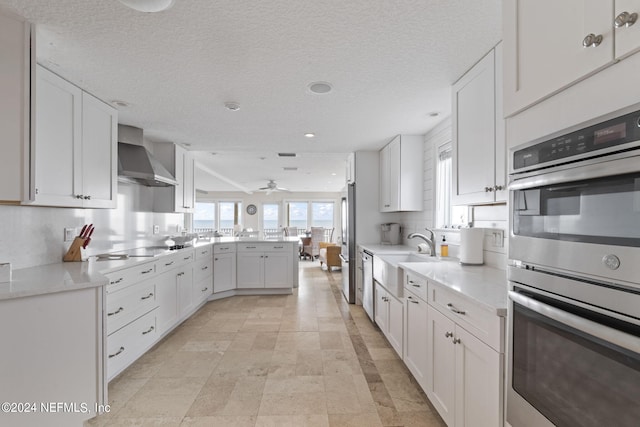 kitchen featuring a peninsula, a sink, stainless steel appliances, light countertops, and wall chimney exhaust hood