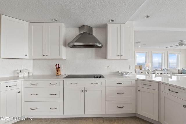 kitchen with wall chimney range hood, white cabinets, light countertops, black electric stovetop, and ceiling fan