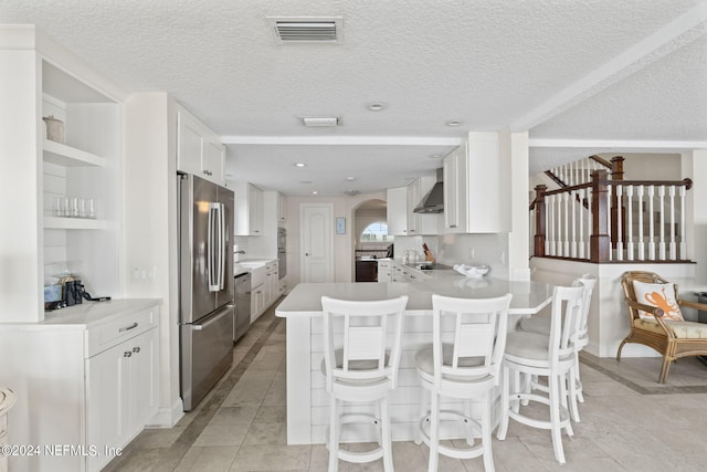 kitchen with kitchen peninsula, white cabinets, a breakfast bar area, appliances with stainless steel finishes, and wall chimney exhaust hood