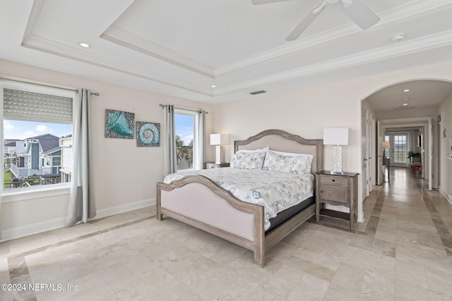 bedroom featuring multiple windows, a raised ceiling, arched walkways, and baseboards