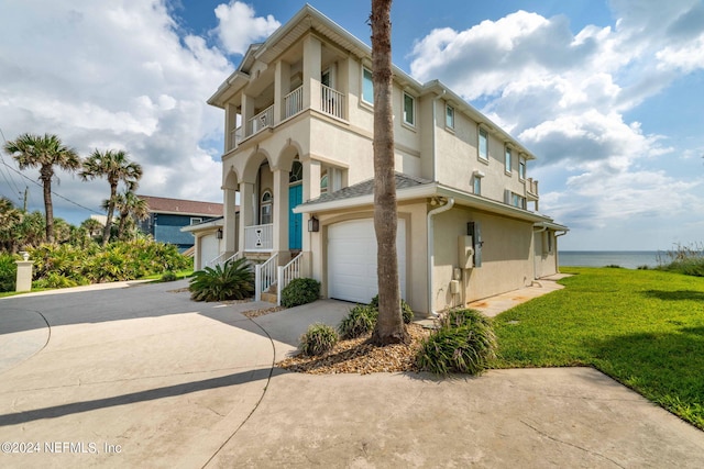 exterior space with a water view, concrete driveway, stucco siding, a lawn, and a balcony