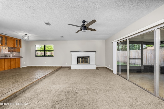 unfurnished living room featuring a textured ceiling, a brick fireplace, ceiling fan, and carpet floors