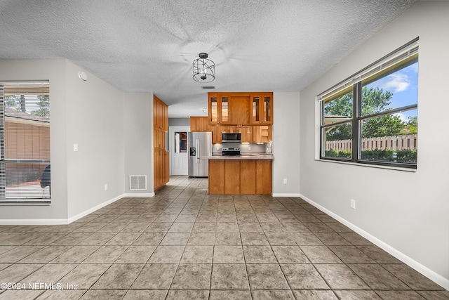 kitchen with a textured ceiling, stainless steel appliances, light tile patterned floors, and kitchen peninsula