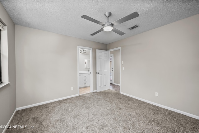 unfurnished bedroom featuring ceiling fan, ensuite bathroom, light carpet, and a textured ceiling