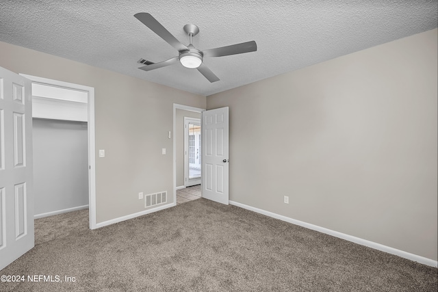 unfurnished bedroom with light carpet, a textured ceiling, ceiling fan, a closet, and a spacious closet