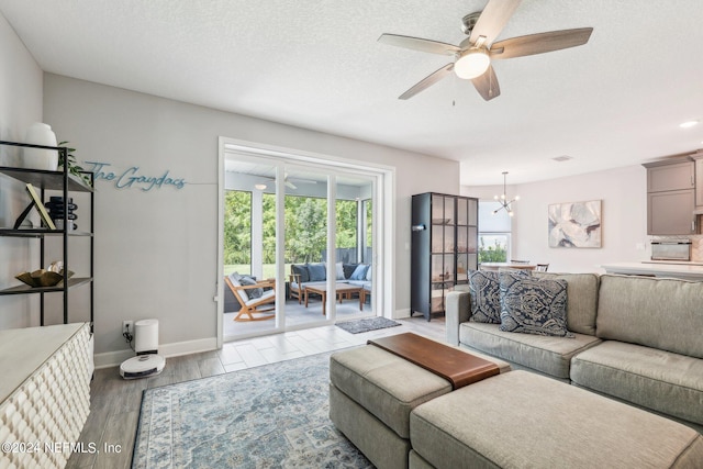 living room with ceiling fan with notable chandelier, light wood-type flooring, and a textured ceiling