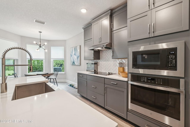 kitchen featuring an inviting chandelier, light hardwood / wood-style flooring, stainless steel appliances, and a textured ceiling