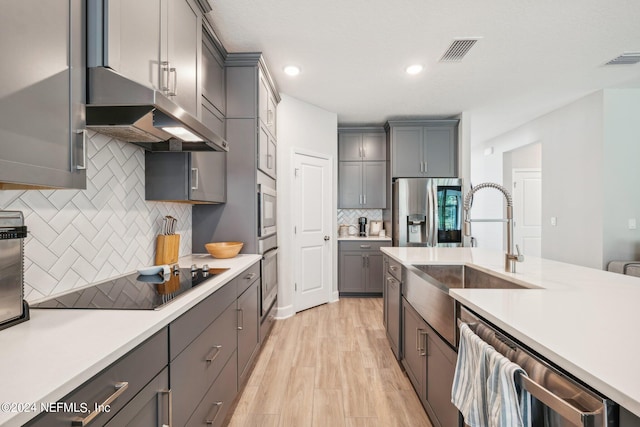 kitchen with gray cabinets, appliances with stainless steel finishes, decorative backsplash, and light hardwood / wood-style flooring