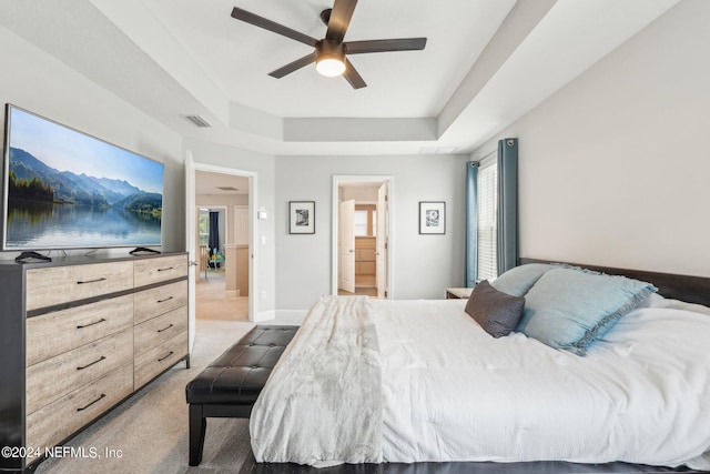 bedroom with a raised ceiling, connected bathroom, ceiling fan, and carpet