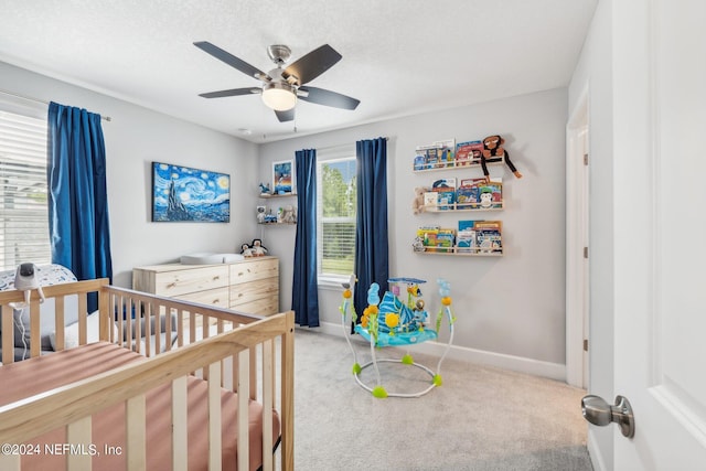 carpeted bedroom featuring ceiling fan, a textured ceiling, and a crib