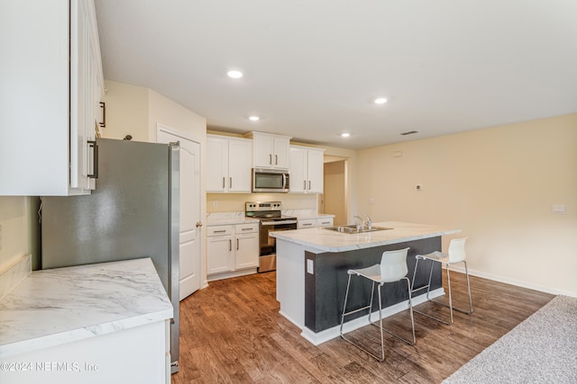 kitchen featuring a breakfast bar area, wood finished floors, a sink, stainless steel appliances, and white cabinets