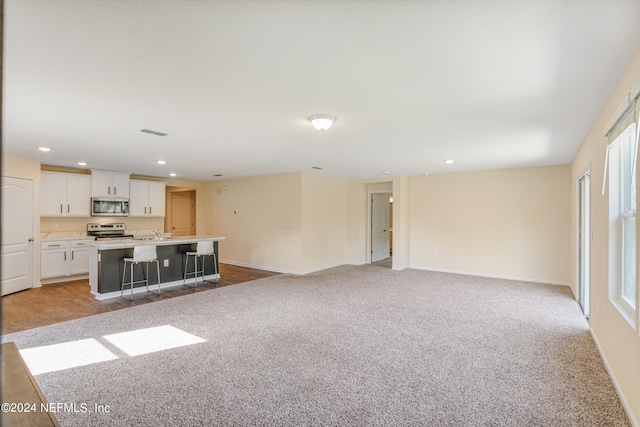 unfurnished living room with recessed lighting, light colored carpet, baseboards, and a sink