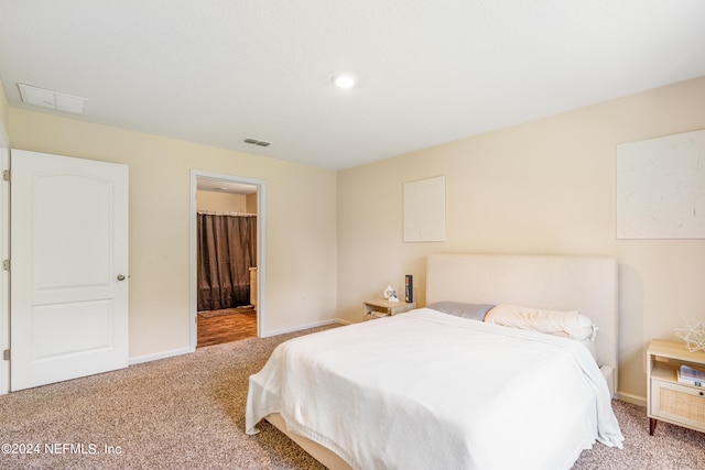 carpeted bedroom with visible vents, ensuite bathroom, and baseboards