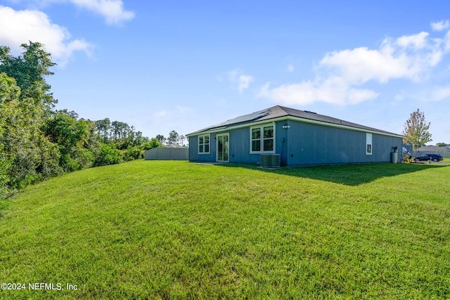 back of property featuring roof mounted solar panels, central air condition unit, and a yard