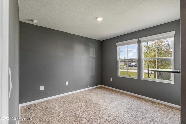 empty room with carpet flooring, baseboards, and a textured ceiling