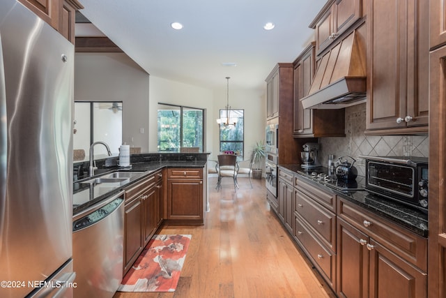 kitchen featuring dark stone countertops, custom range hood, light hardwood / wood-style flooring, appliances with stainless steel finishes, and sink