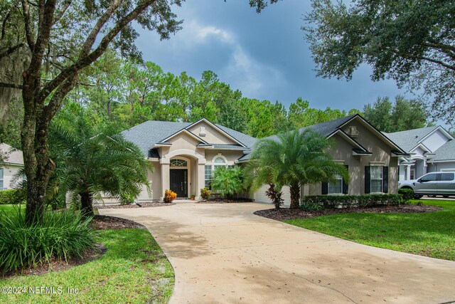 view of front facade with an attached garage, a shingled roof, driveway, stucco siding, and a front yard