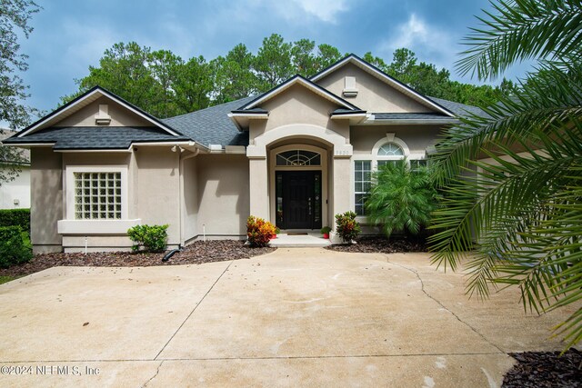 ranch-style house featuring a shingled roof and stucco siding