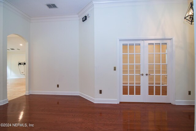 unfurnished room featuring baseboards, arched walkways, wood finished floors, crown molding, and french doors