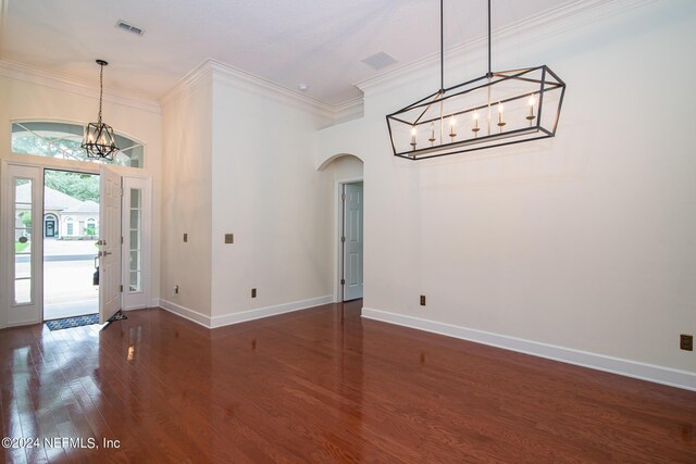 foyer entrance featuring baseboards, crown molding, arched walkways, and wood finished floors