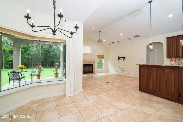 kitchen with light stone counters, visible vents, vaulted ceiling, a tile fireplace, and ceiling fan with notable chandelier