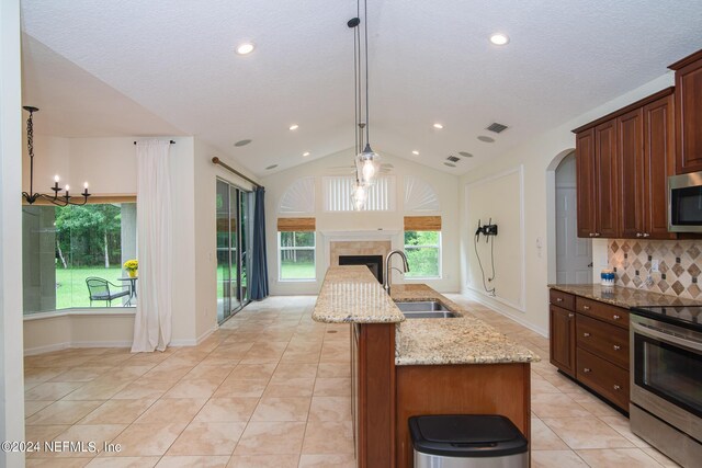 kitchen with tasteful backsplash, an island with sink, stainless steel appliances, a fireplace, and a sink