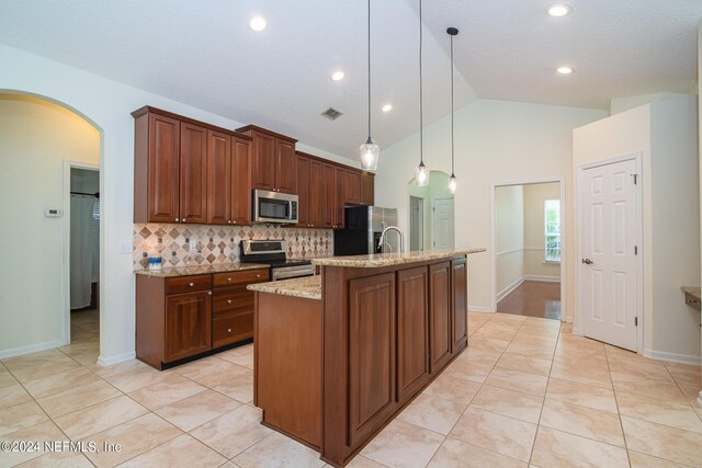 kitchen with tasteful backsplash, arched walkways, an island with sink, appliances with stainless steel finishes, and vaulted ceiling