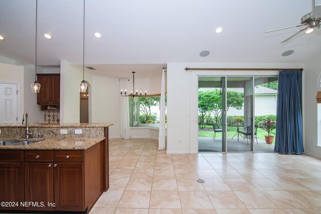 kitchen with hanging light fixtures, light stone countertops, ceiling fan with notable chandelier, a sink, and recessed lighting