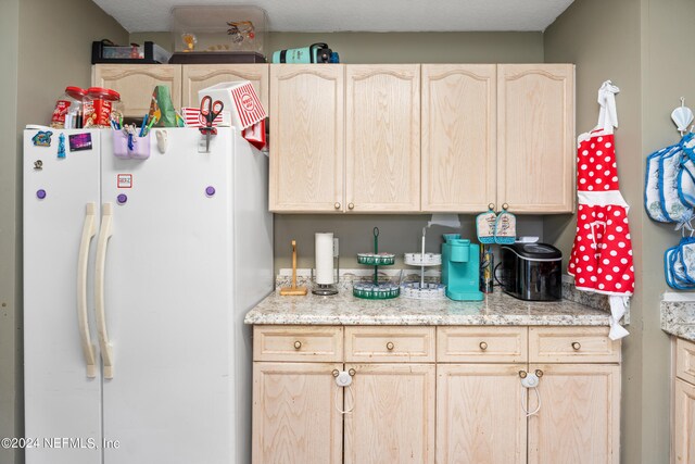 kitchen with white refrigerator, a textured ceiling, light stone counters, and light brown cabinets