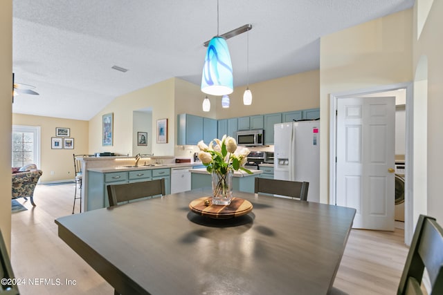 dining room featuring ceiling fan, a textured ceiling, light wood-type flooring, vaulted ceiling, and sink