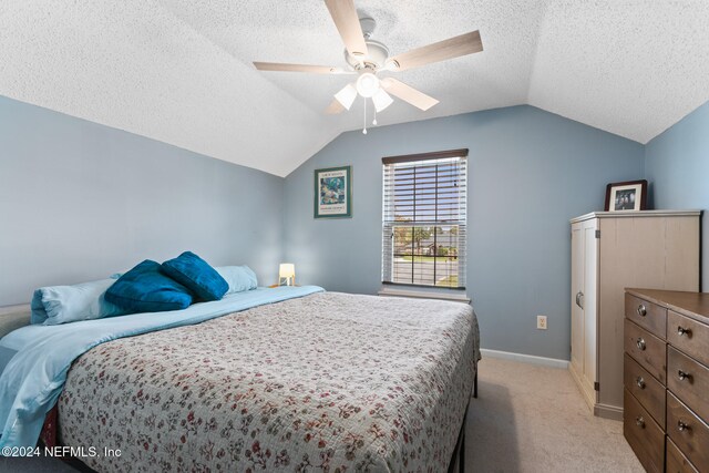 bedroom with a textured ceiling, light colored carpet, vaulted ceiling, and ceiling fan