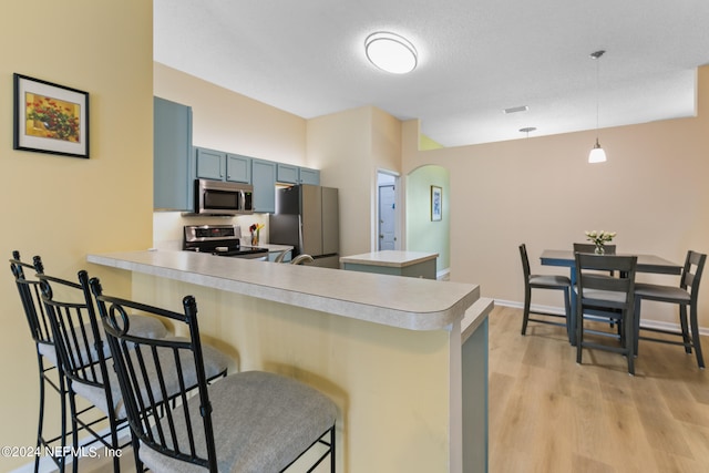 kitchen featuring appliances with stainless steel finishes, a breakfast bar, decorative light fixtures, and kitchen peninsula