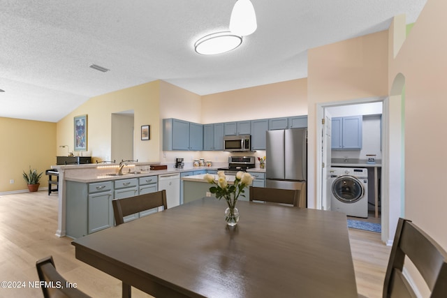 dining space featuring washer / dryer, sink, light wood-type flooring, a textured ceiling, and vaulted ceiling