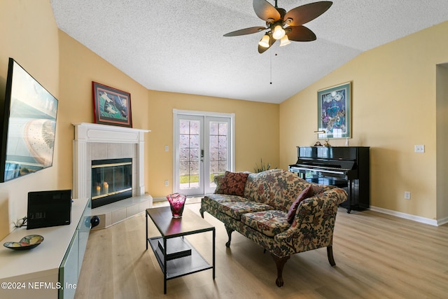 living room with light wood-type flooring, a textured ceiling, a tiled fireplace, ceiling fan, and vaulted ceiling