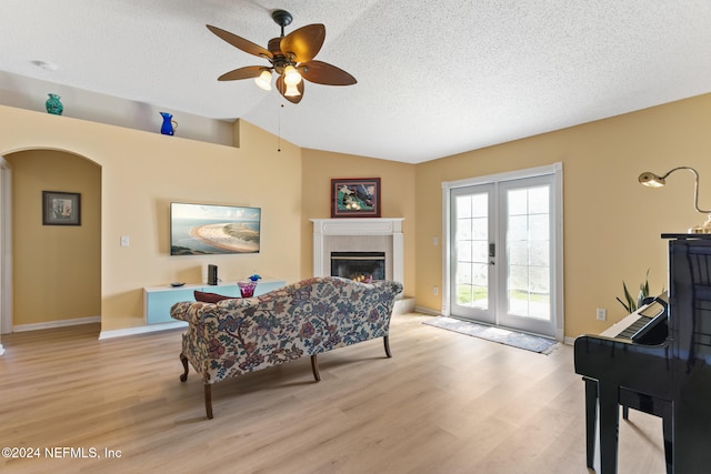 living room featuring lofted ceiling, light hardwood / wood-style flooring, a tile fireplace, a textured ceiling, and ceiling fan