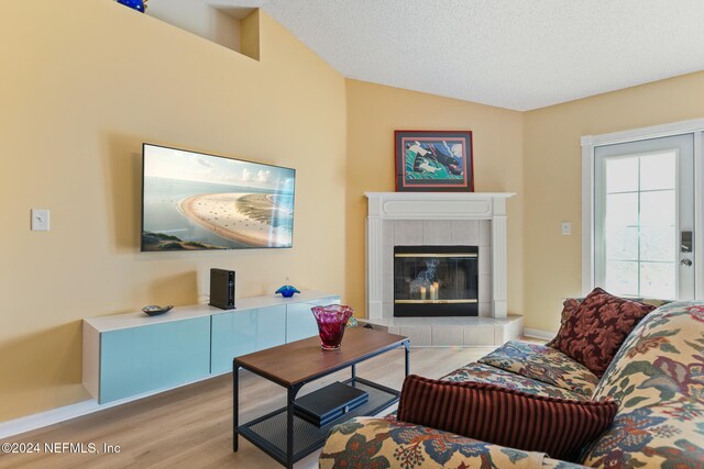 living room with a textured ceiling, a tiled fireplace, light wood-type flooring, and vaulted ceiling