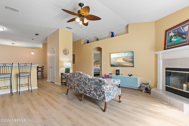 living room with a textured ceiling, light hardwood / wood-style flooring, a fireplace, and ceiling fan