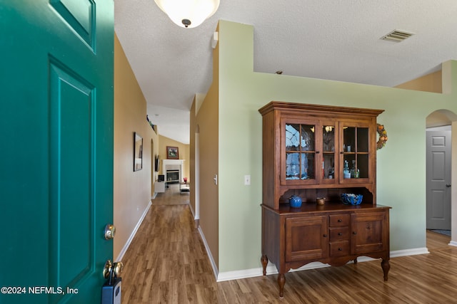 corridor with hardwood / wood-style floors, a textured ceiling, and vaulted ceiling