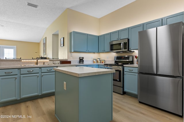 kitchen featuring a textured ceiling, stainless steel appliances, light wood-type flooring, and a kitchen island