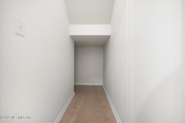 corridor with light tile patterned floors, a textured ceiling, and baseboards