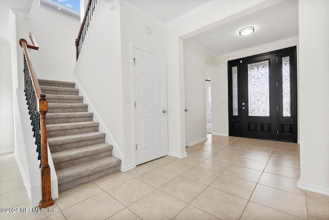 foyer entrance featuring light tile patterned floors, baseboards, ornamental molding, and a textured ceiling