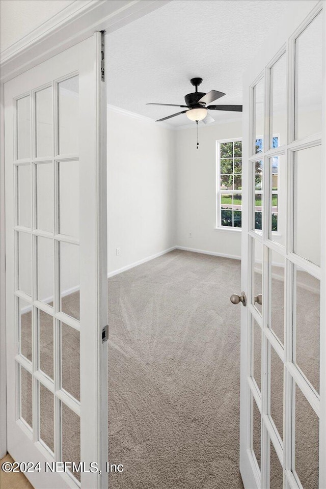 empty room featuring a textured ceiling, carpet flooring, a ceiling fan, baseboards, and french doors